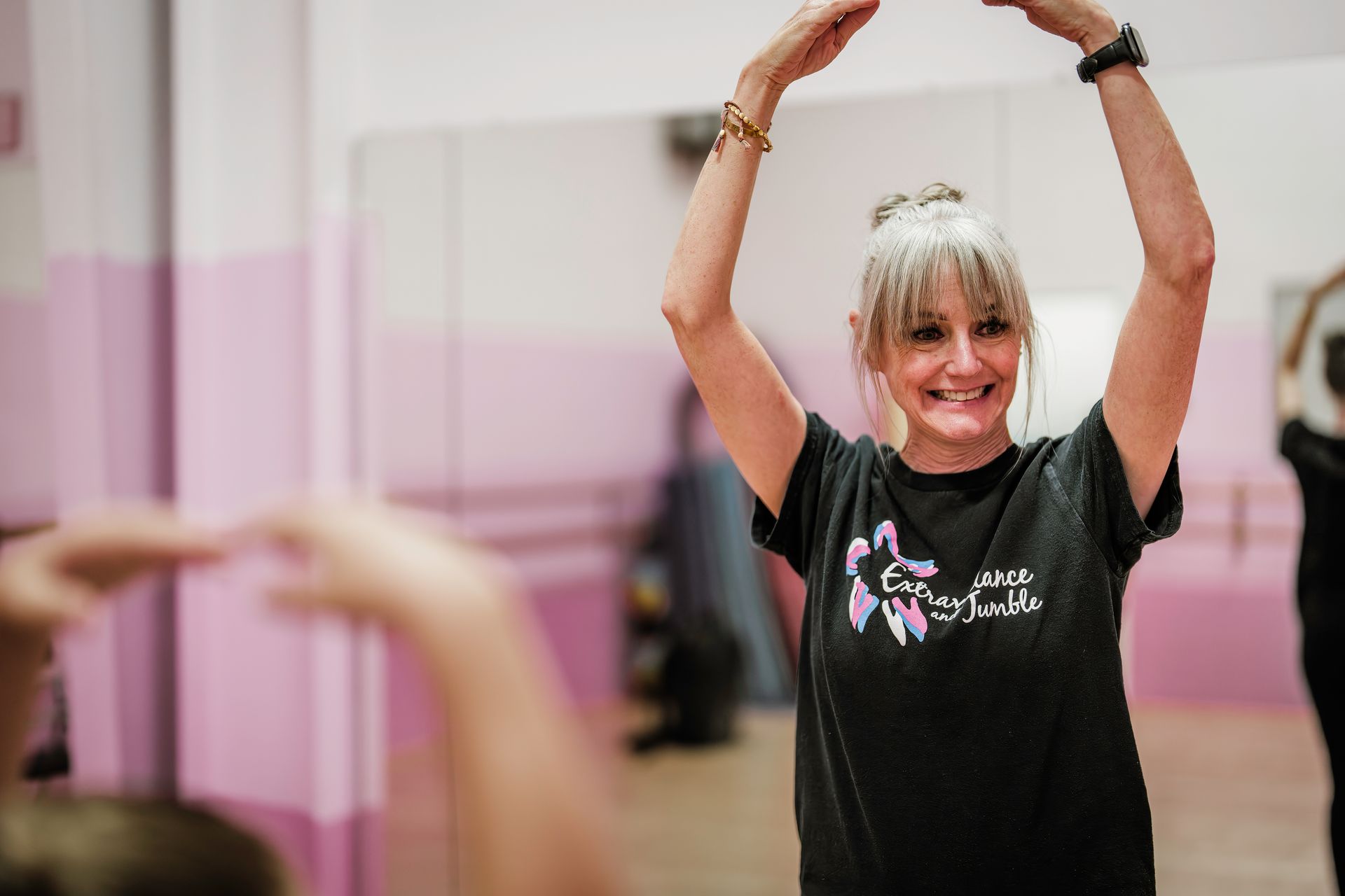 Woman in a black shirt stretching with arms overhead in a pink studio