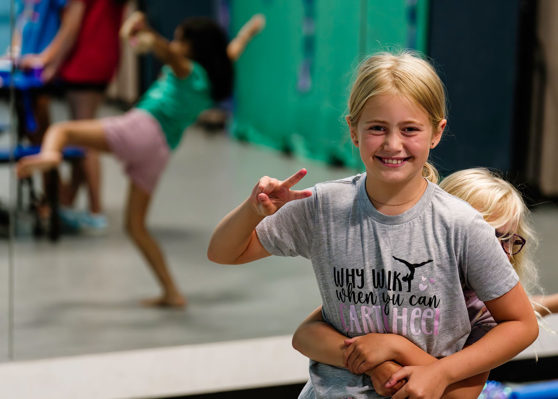 Smiling child in a gray shirt posing indoors, with a blurred dance class in the background