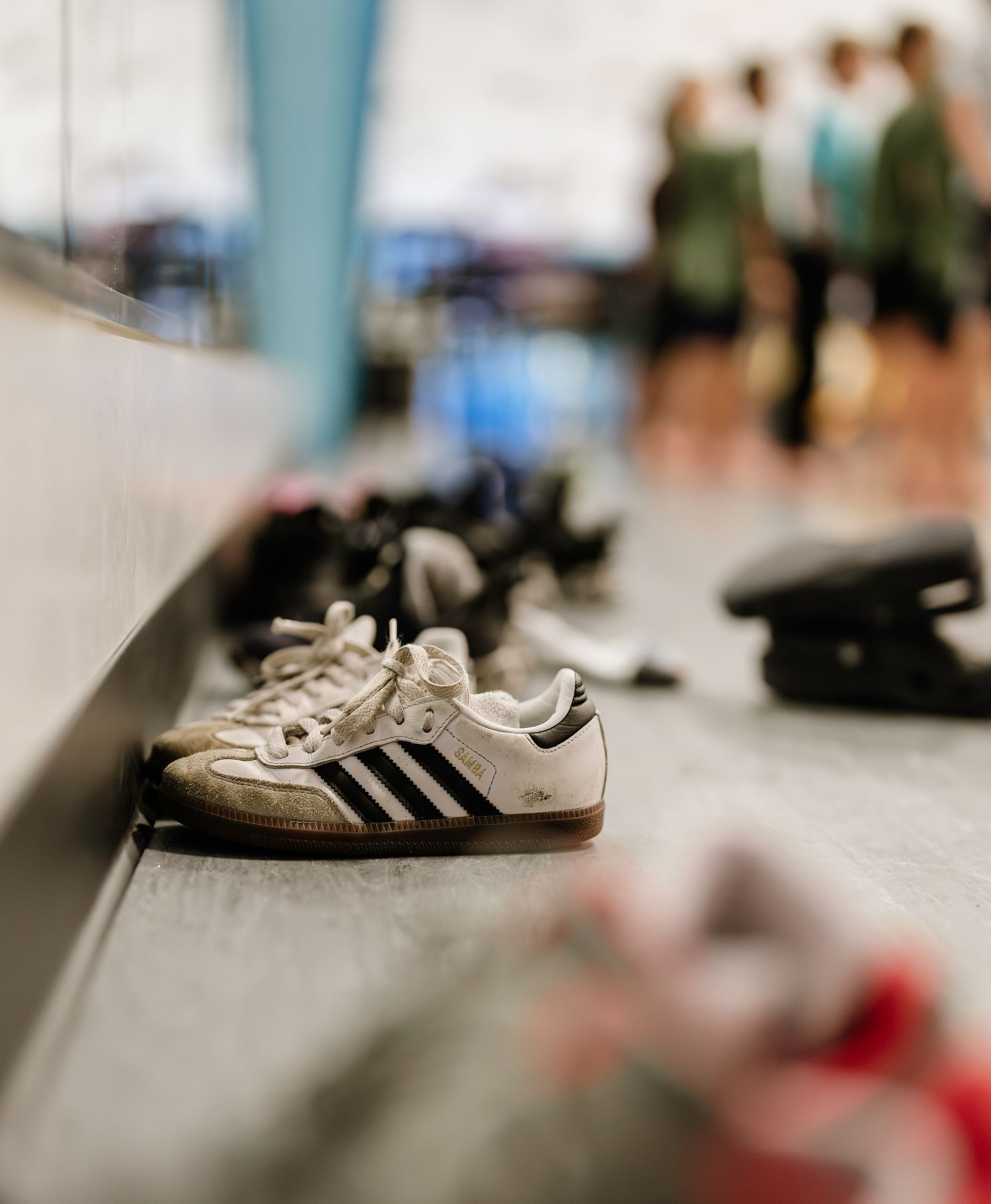 White Adidas sneaker on a gym floor with blurred people in the background