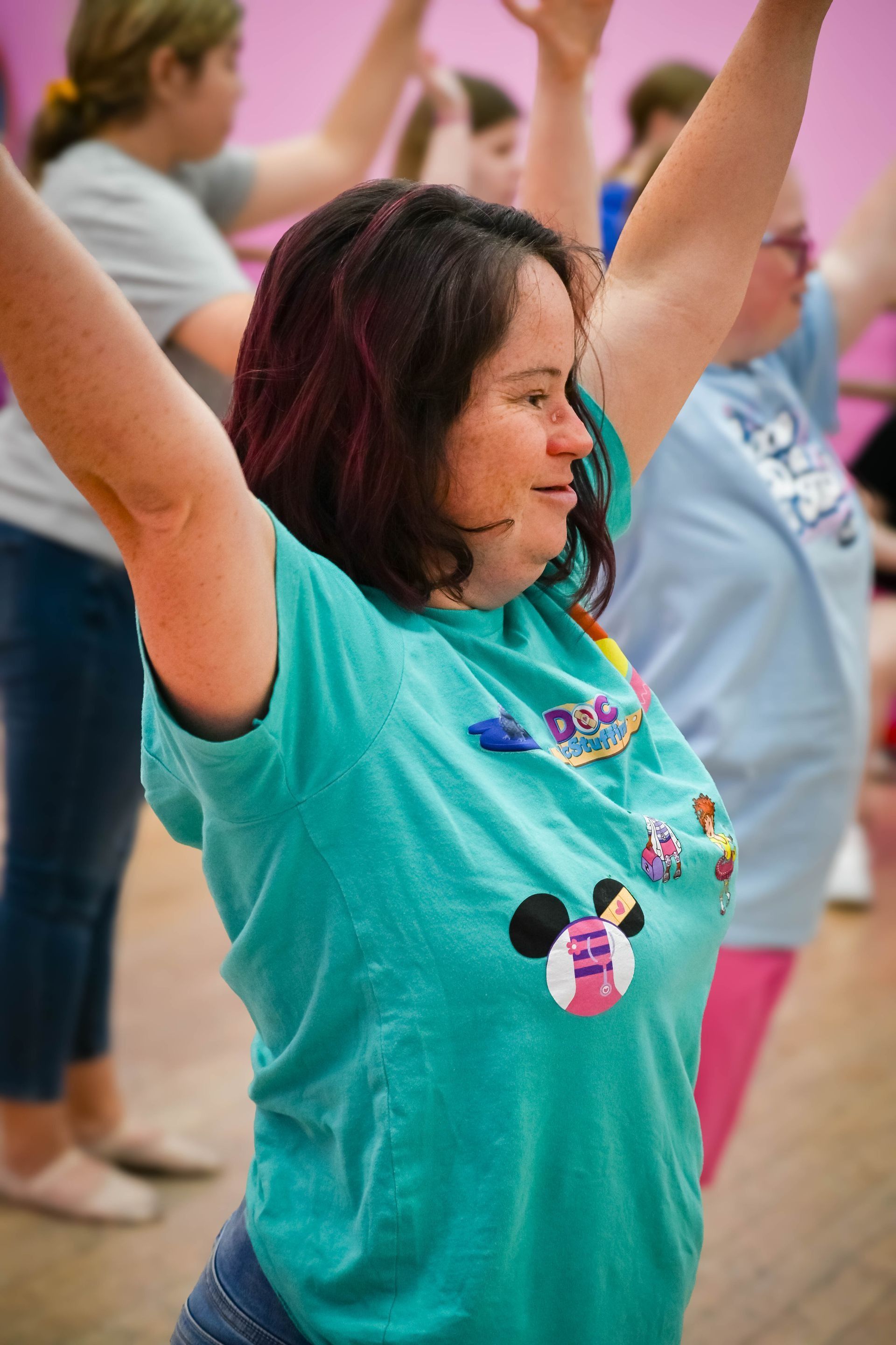 Woman in a turquoise shirt raising her arms during an exercise class