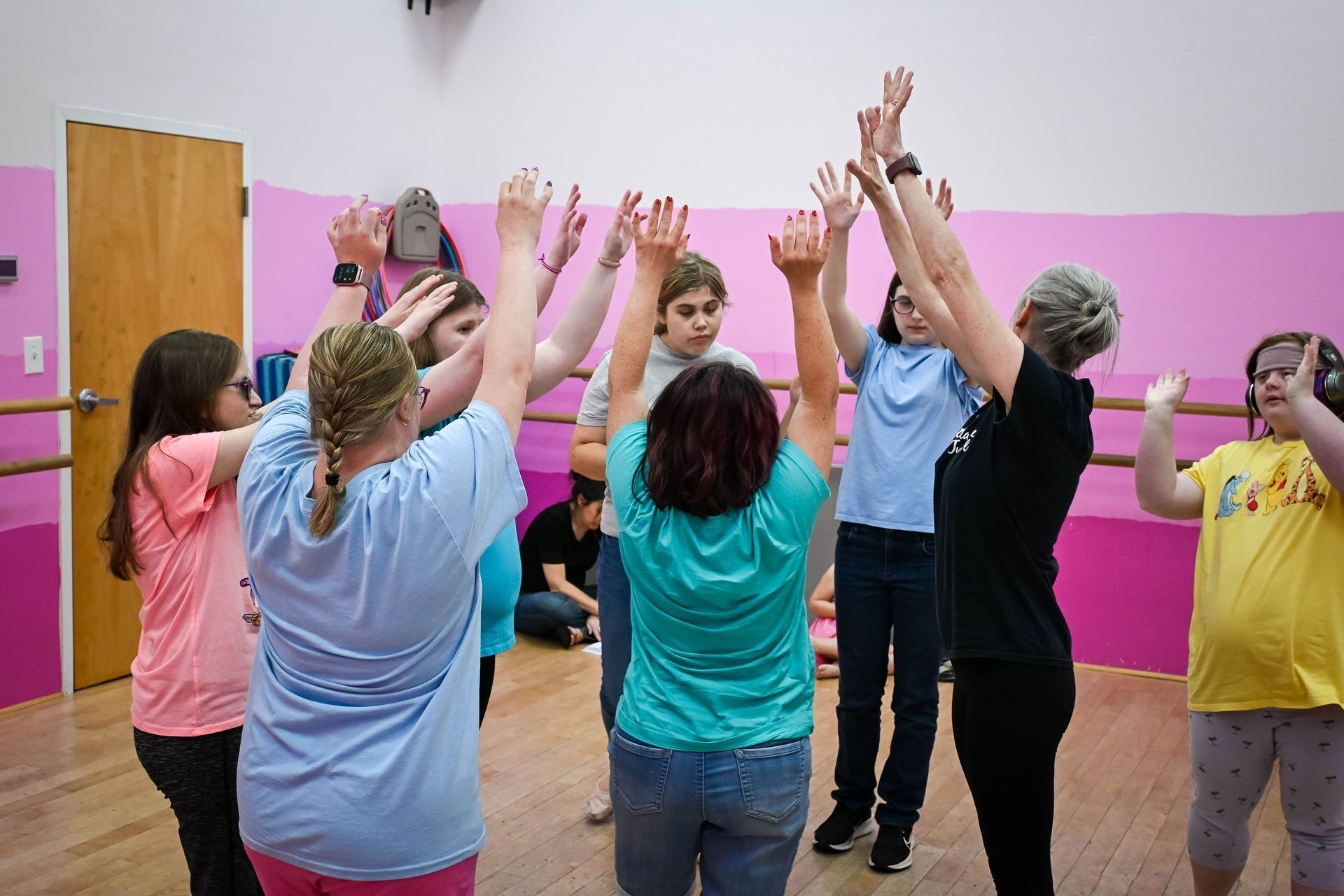 Group of people in a studio raising their arms in a circle, facing a leader in a black shirt