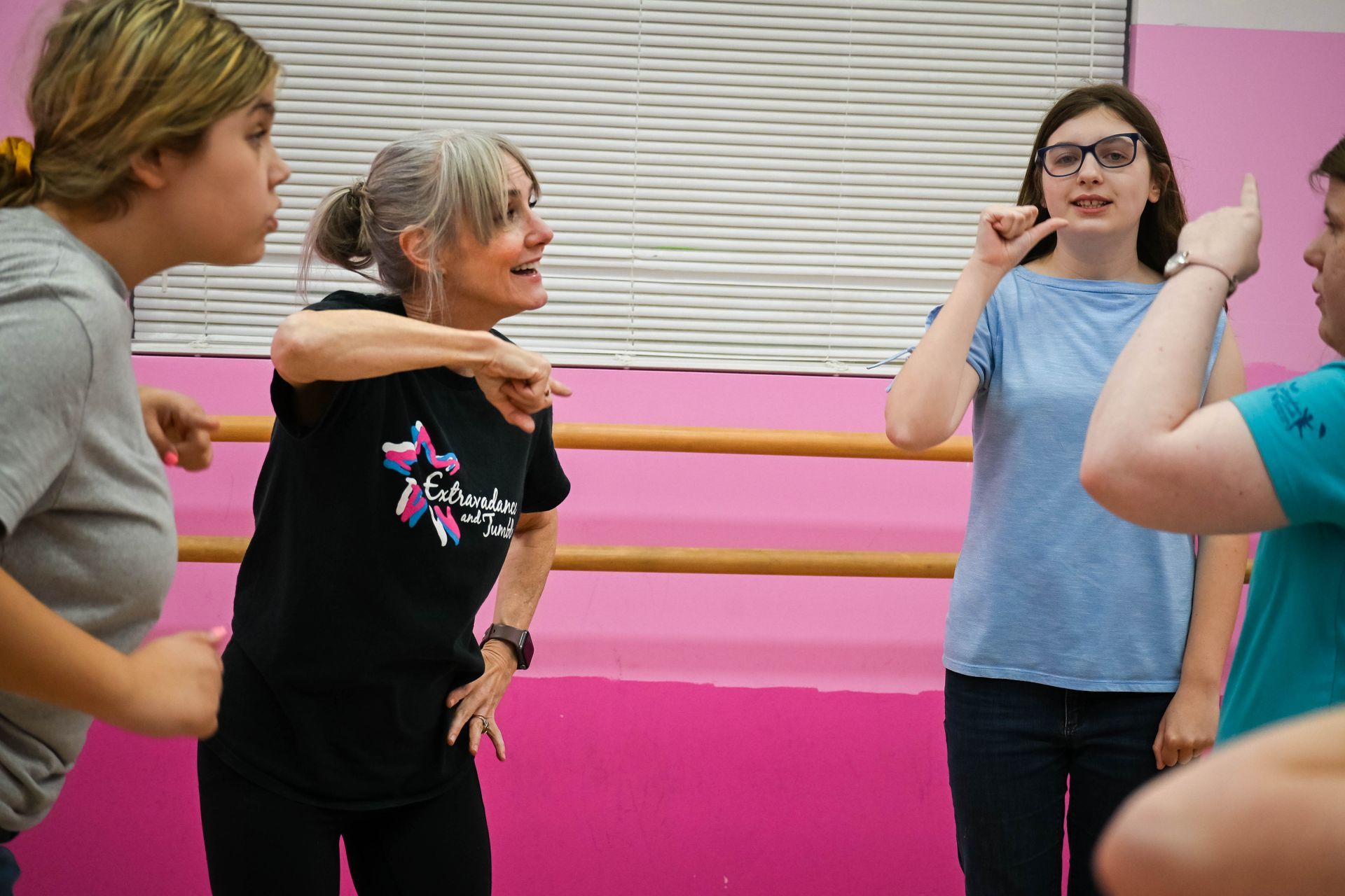 People stretching in a pink dance studio, with an instructor guiding them.