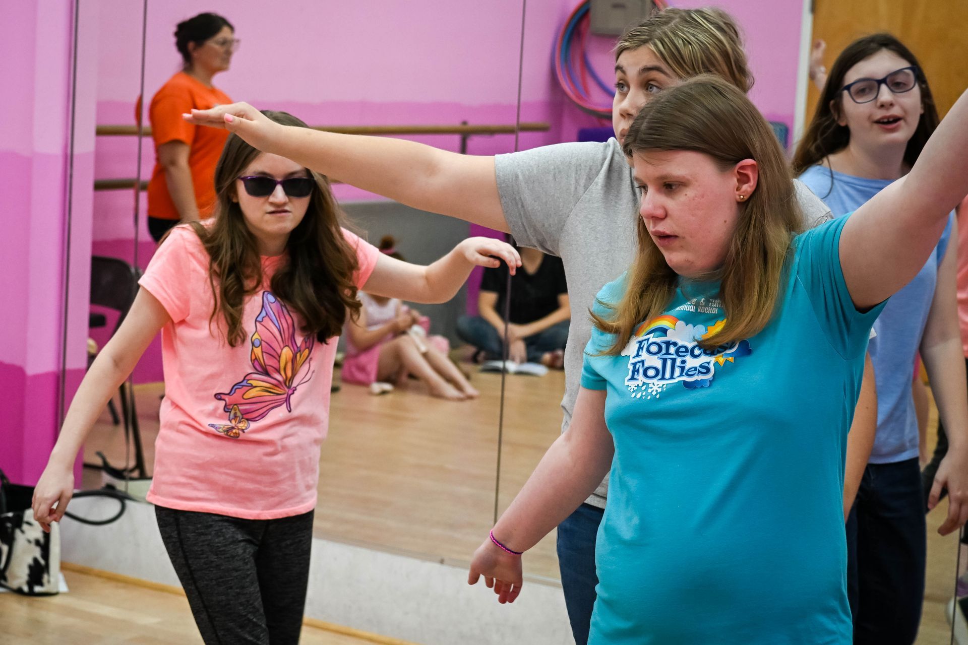 People practicing dance stretches in a pink studio, arms extended in front of a mirror.