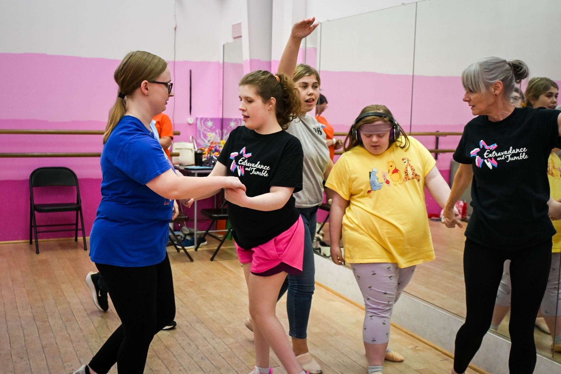 People practicing a dance routine in a studio with pink walls and a wooden floor