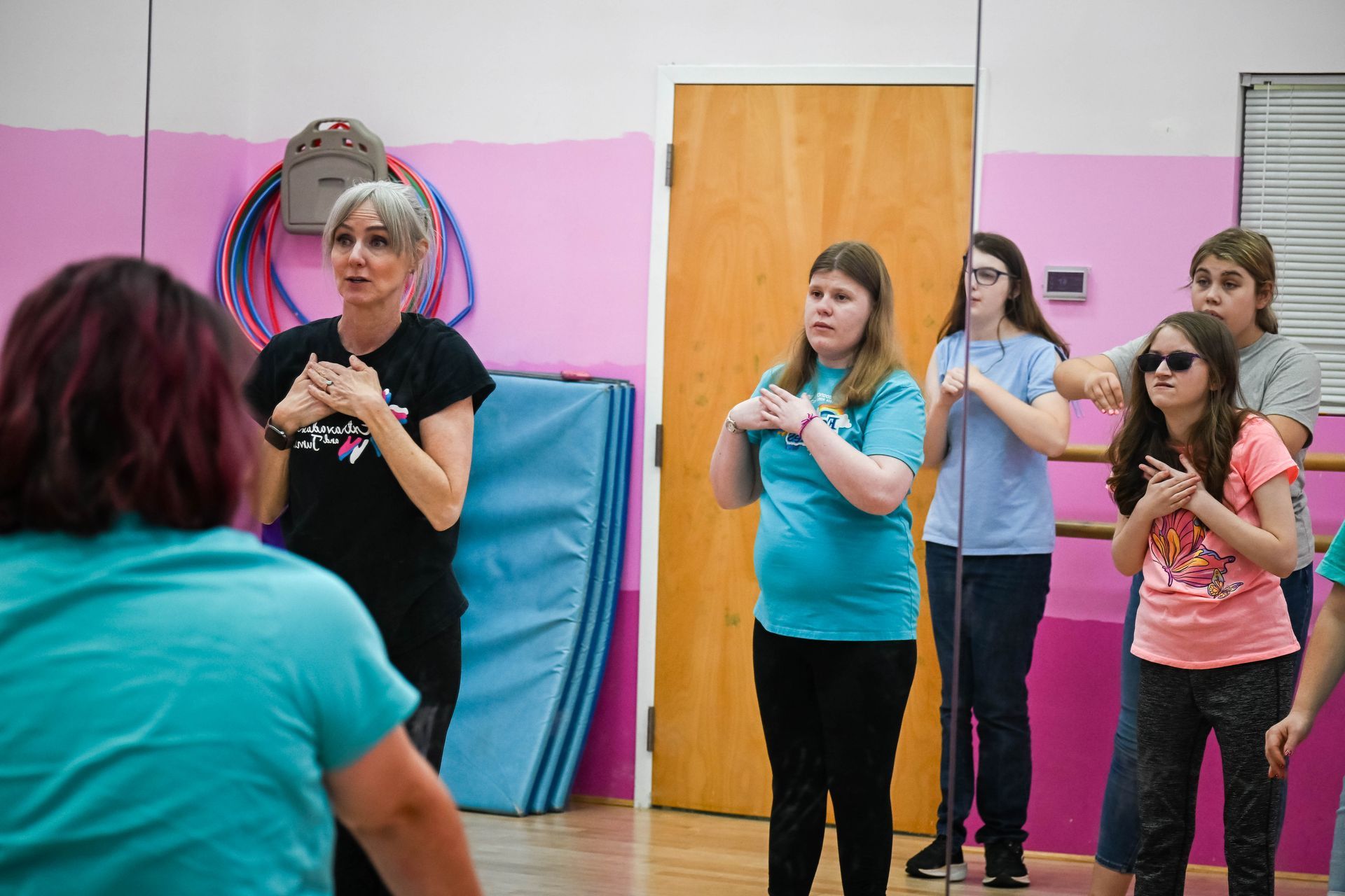 People standing in a studio, watching a woman demonstrate hand movements during an activity class