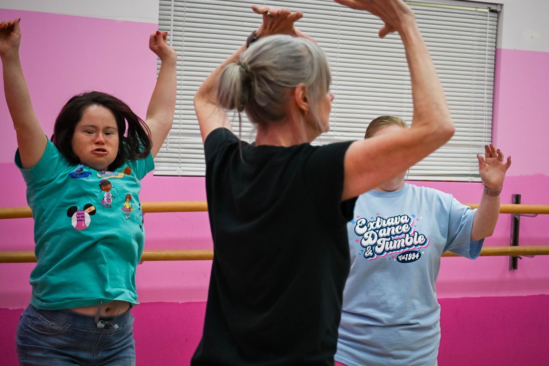 Three people stretching with raised arms in a bright pink dance studio