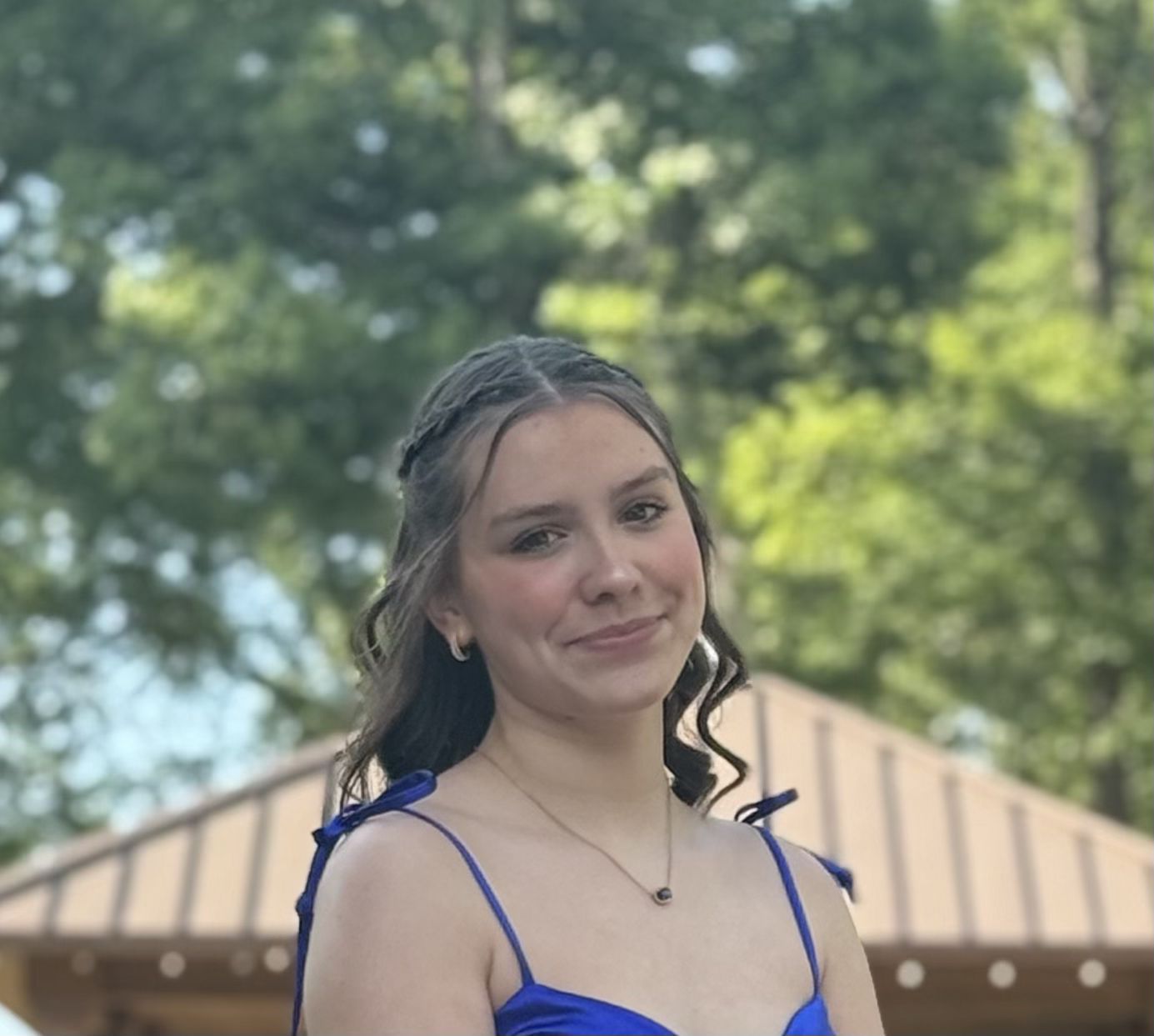 Young person in a blue dress smiling outdoors with trees and a tent in the background