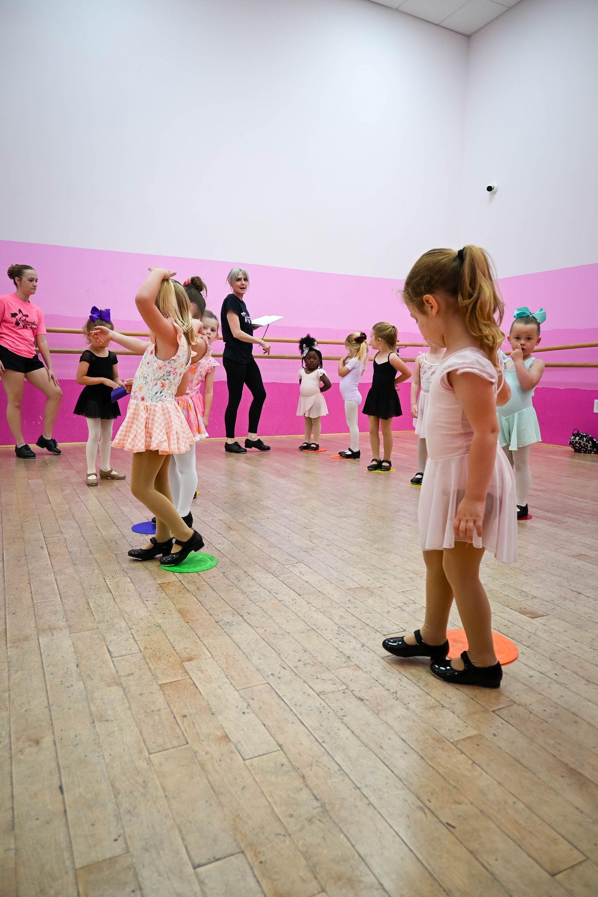 Children in pink dance costumes practicing in a bright studio with a pink wall.