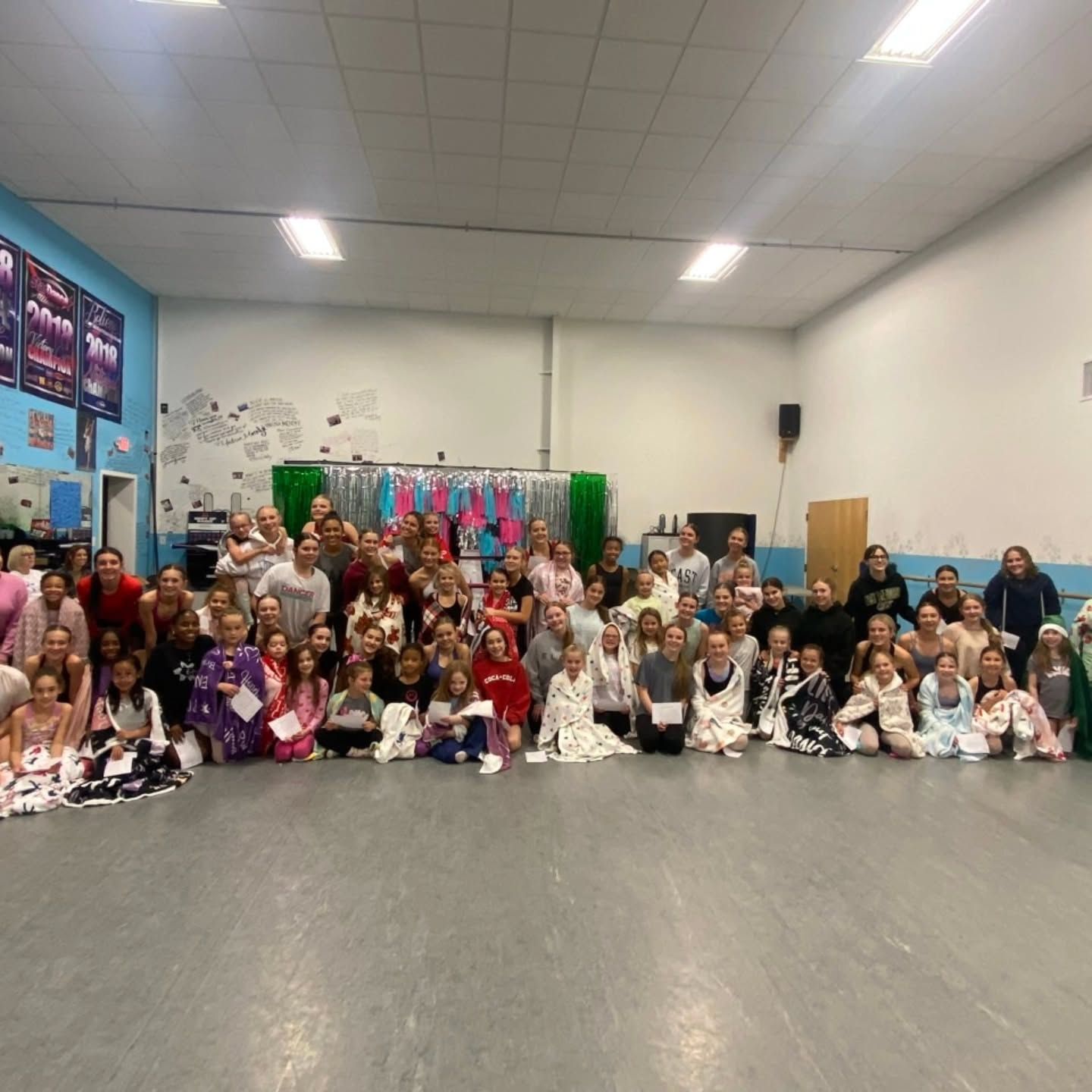 Large group posed in a dance studio with costumes and props against the back wall
