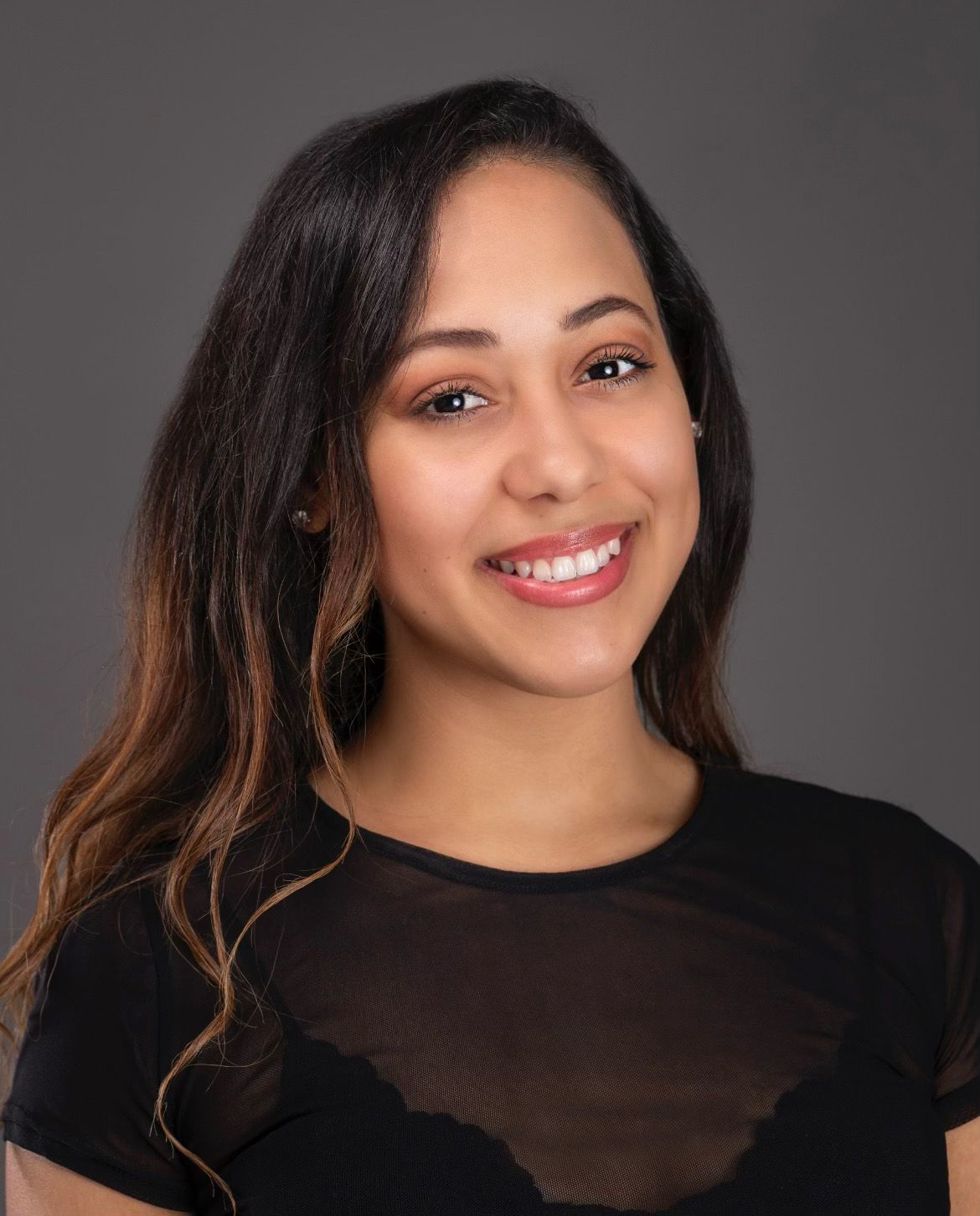 Smiling person with long dark hair wearing a black top against a gray background