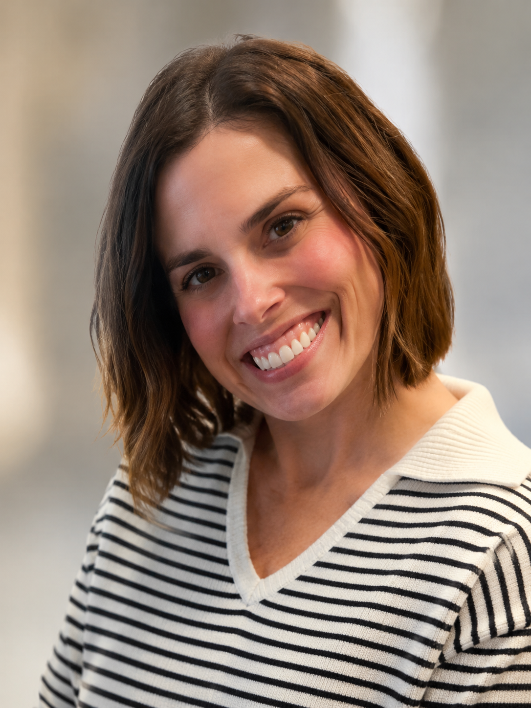 Smiling person in a striped sweater against a softly blurred indoor background