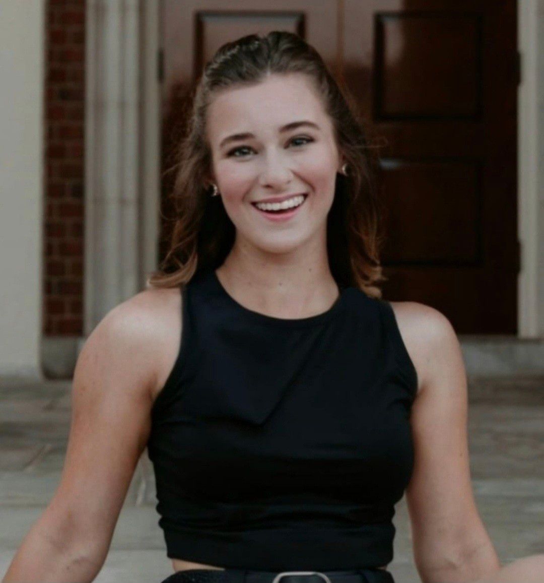 Smiling person in a black sleeveless top sitting on steps outdoors.