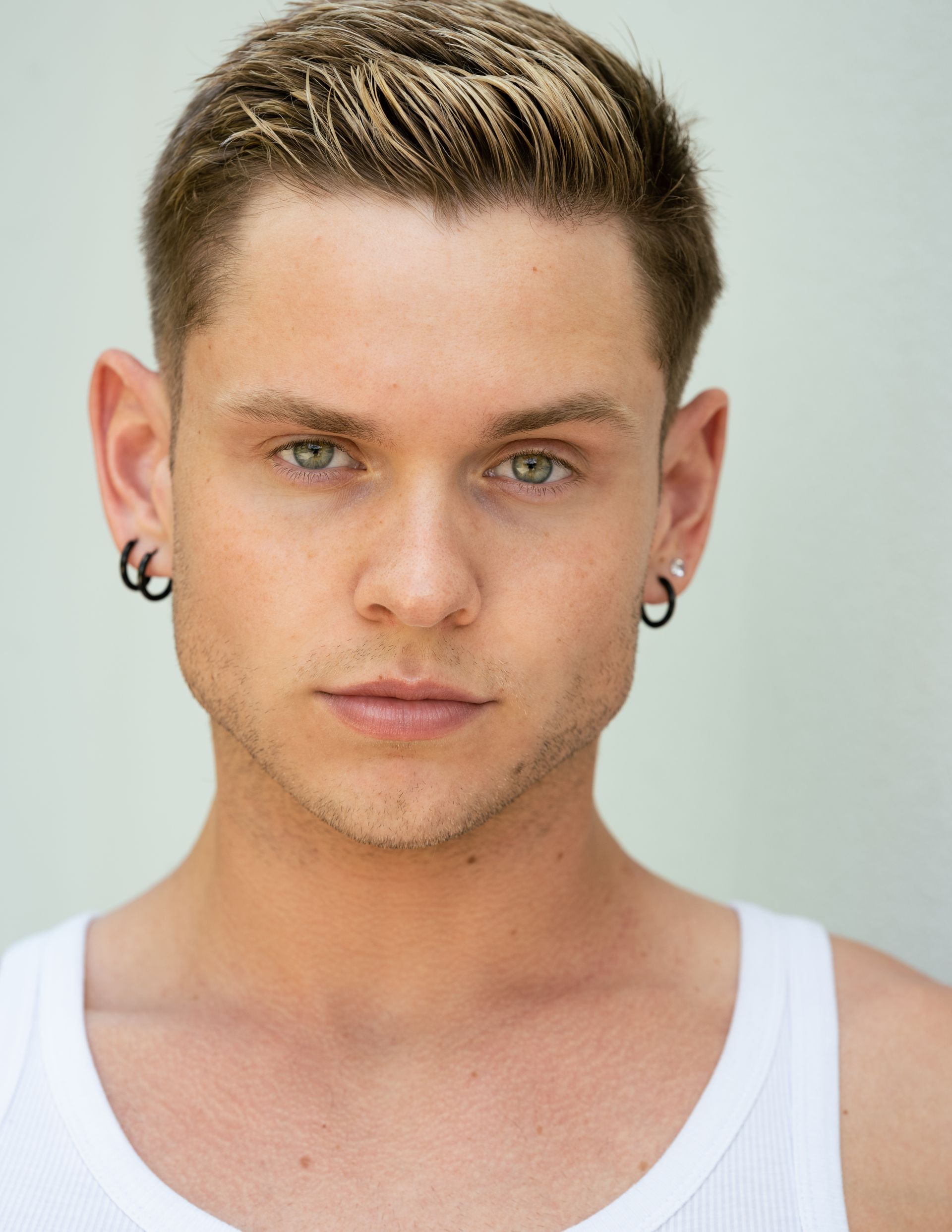 Portrait of a person in a white tank top against a light background, looking straight ahead