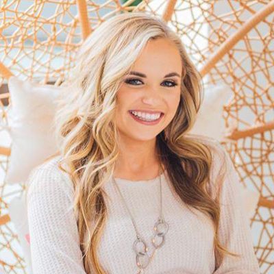 Smiling blonde woman in a light sweater, seated against a woven white and tan backdrop