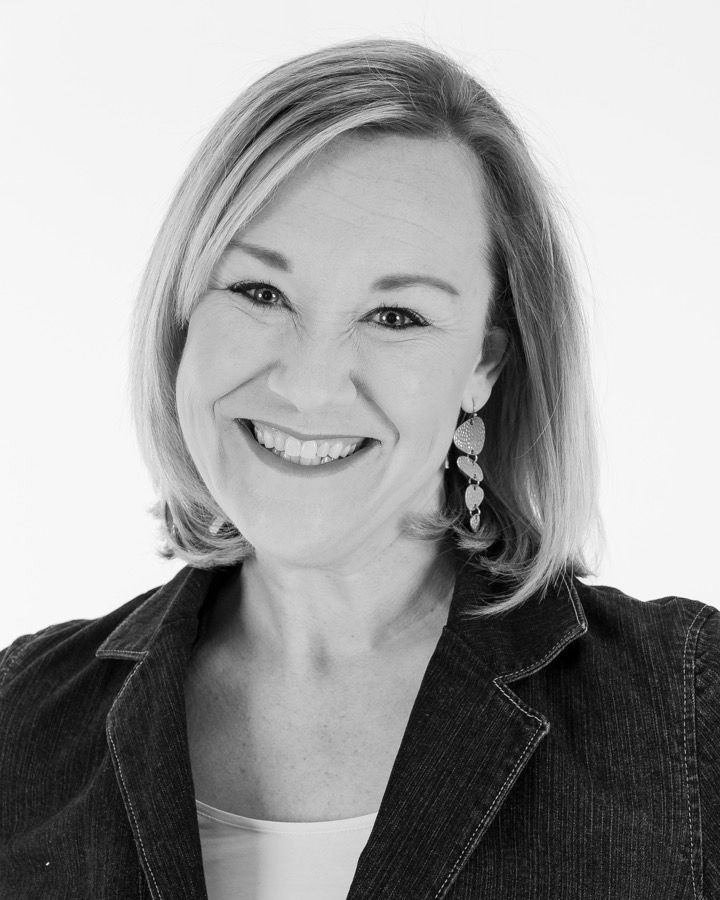 Smiling woman in a dark blazer, photographed against a light background.