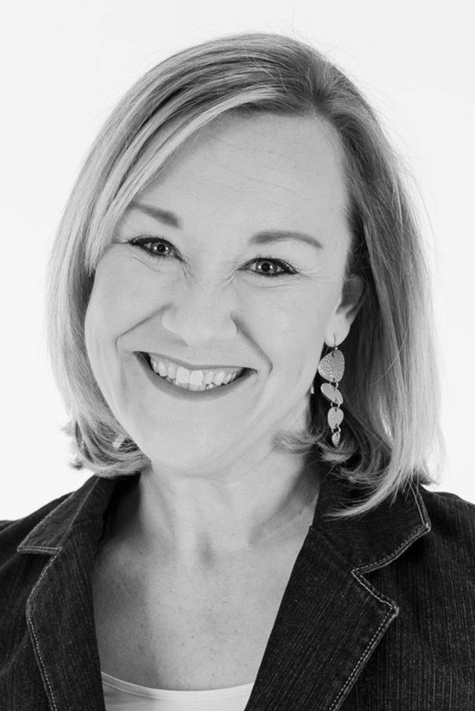 Smiling woman in a dark blazer, photographed against a light background.