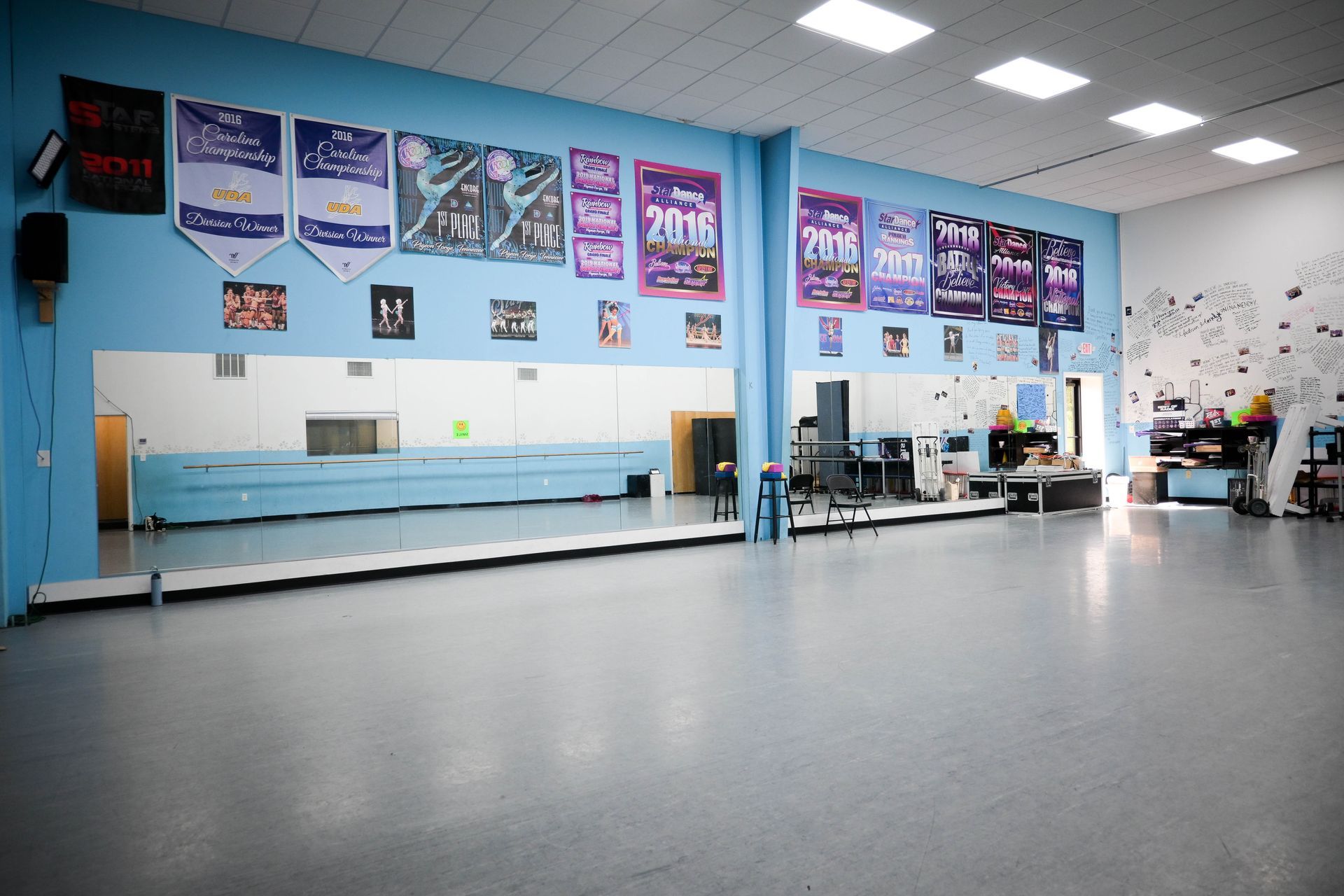 Spacious dance studio with mirrored walls, blue benches, posters, and black dance floor