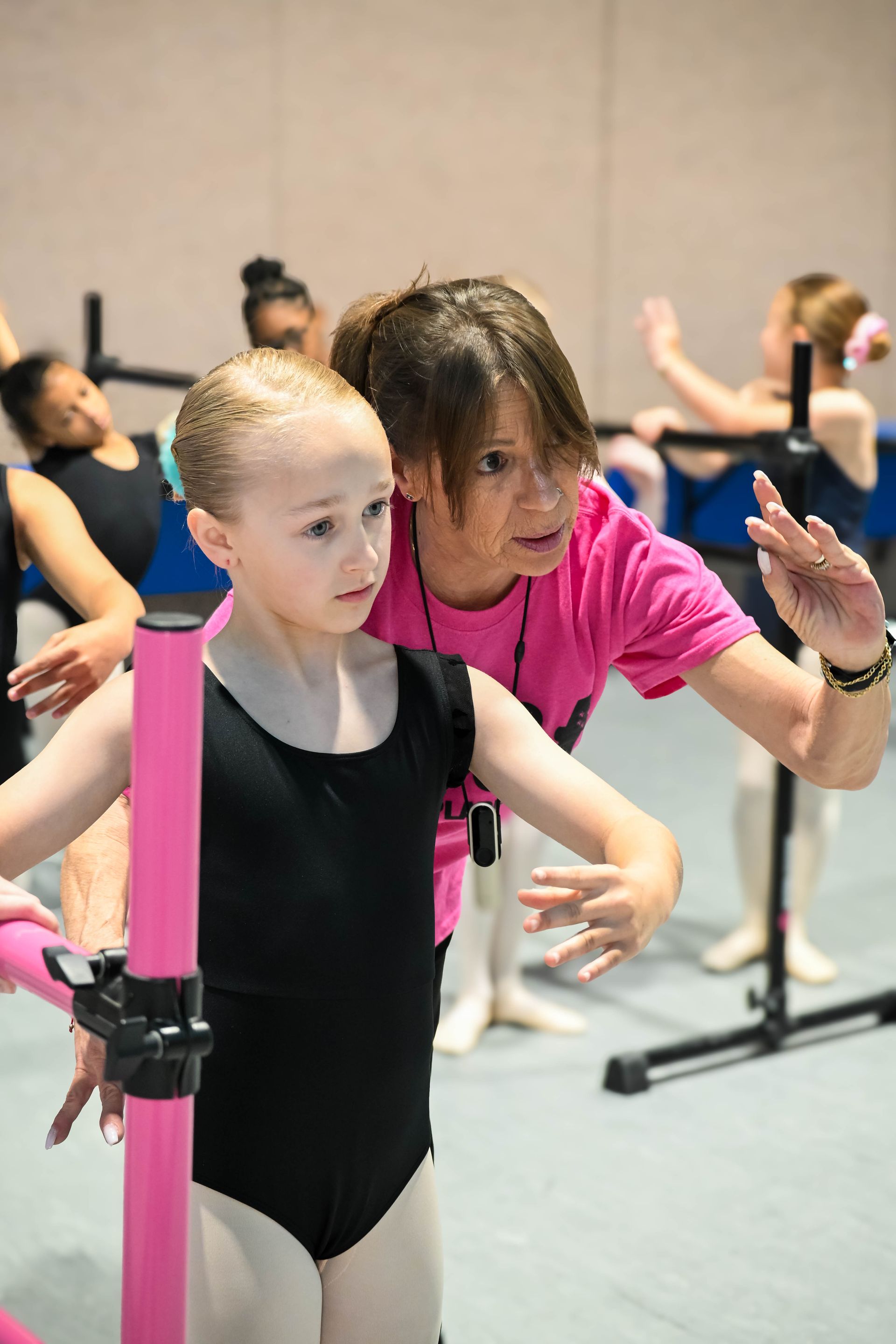 Instructor guiding a child at a pink ballet barre in a dance studio
