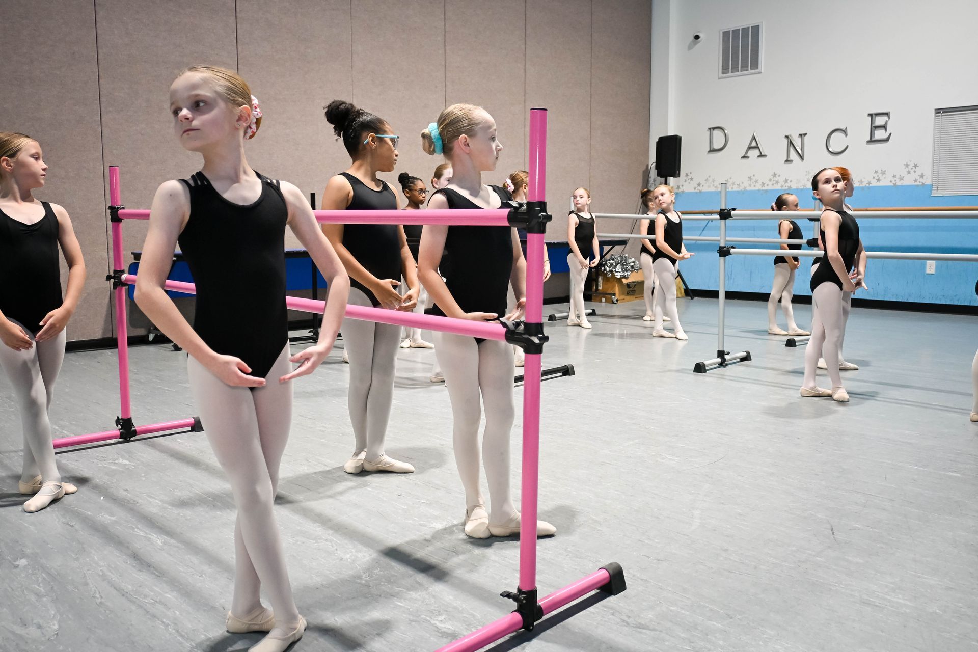 Ballet class practicing at pink barre in a dance studio with mirrors and “DANCE” on the wall