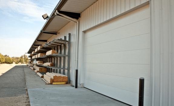A white building with a garage door and shelves of wood