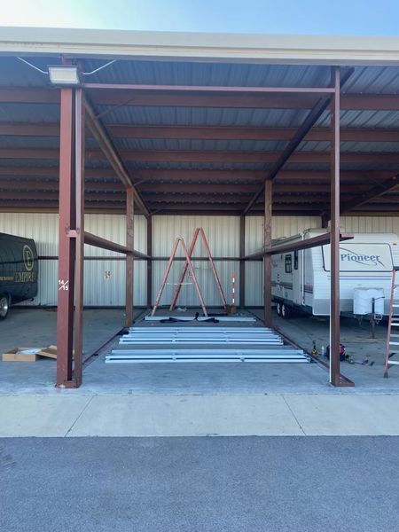 A rv is parked under a metal structure in a parking lot.