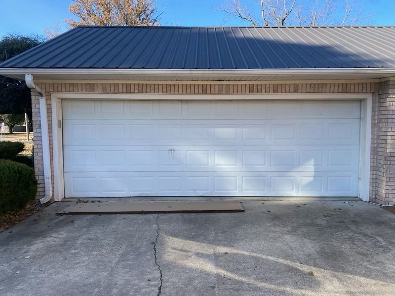 A white garage door with a black roof is sitting in front of a brick house.