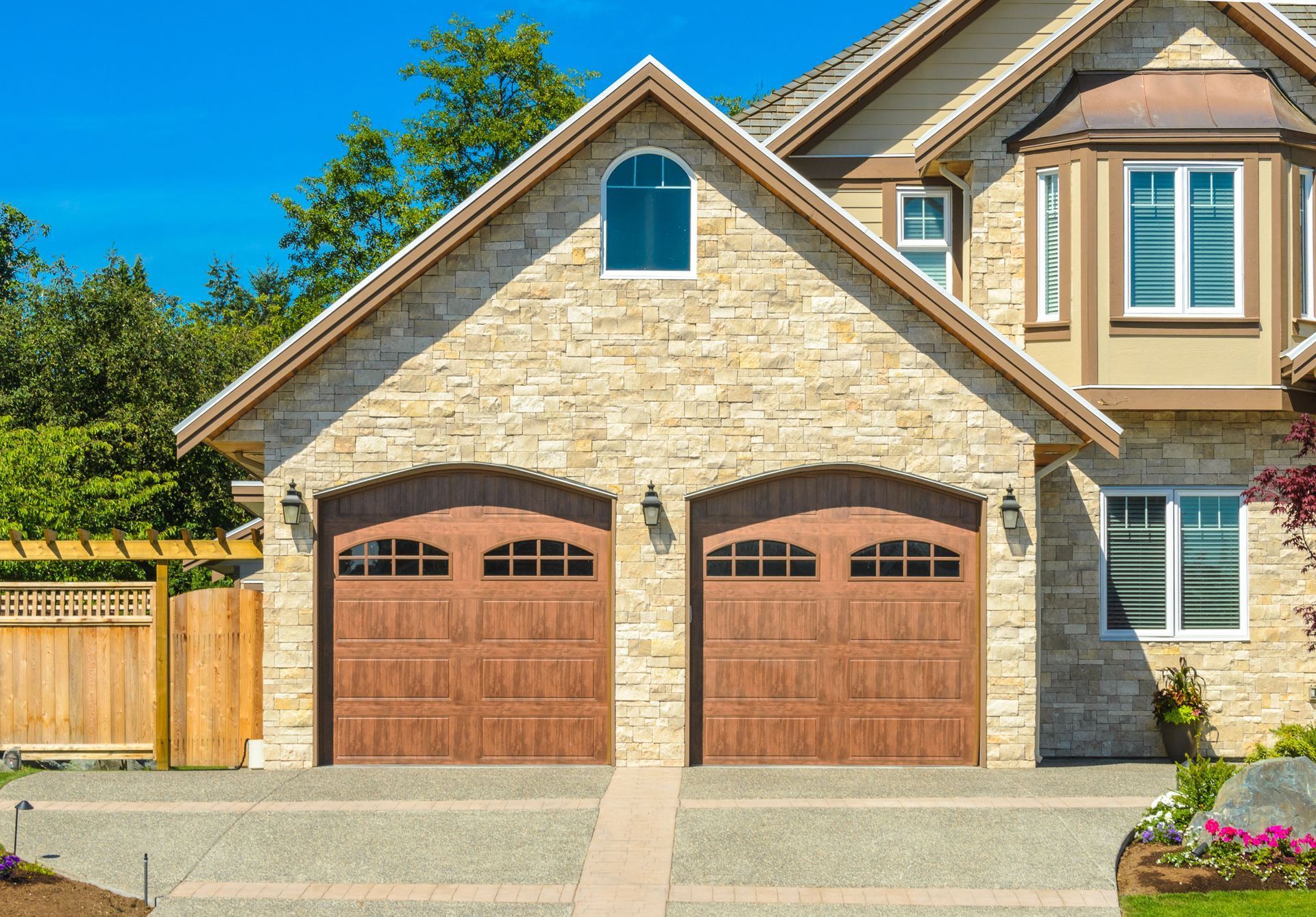 Brown garage doors with stone facade on a house with a blue sky.