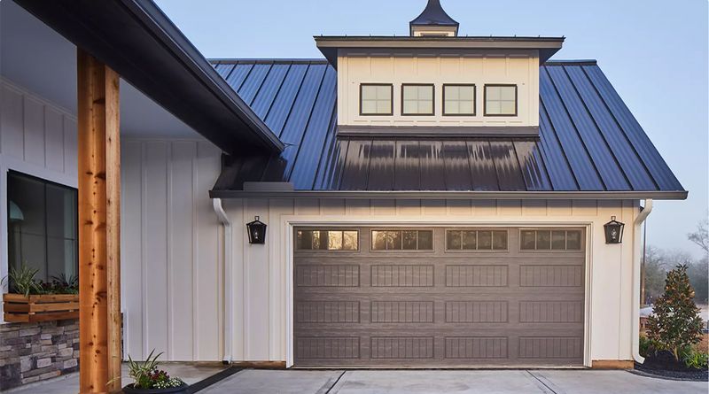 White garage with a dark grey door and black roof, with a small white cupola.
