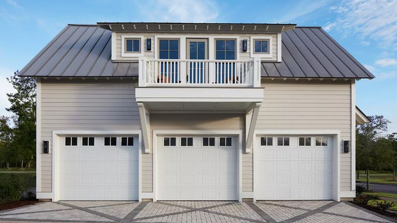 Three-bay garage with white doors, balcony, and gray metal roof; light beige siding.
