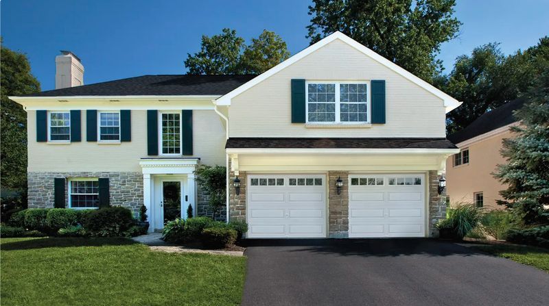 Two-story house with beige siding, stone accents, black roof, and two-car garage.
