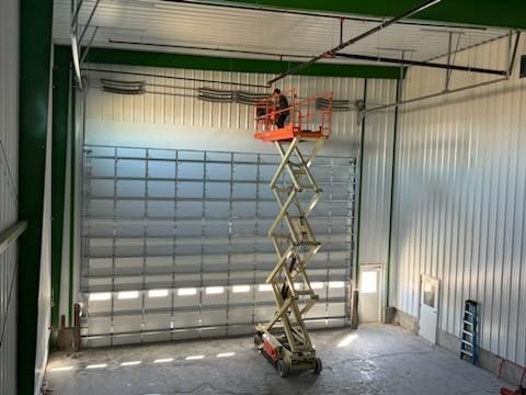 Person on scissor lift works on wiring above a large warehouse door, in a metal building.
