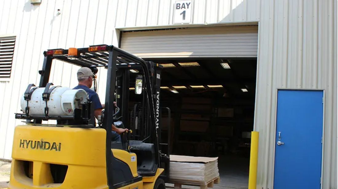 Yellow forklift exiting a warehouse, driven by a person. 
