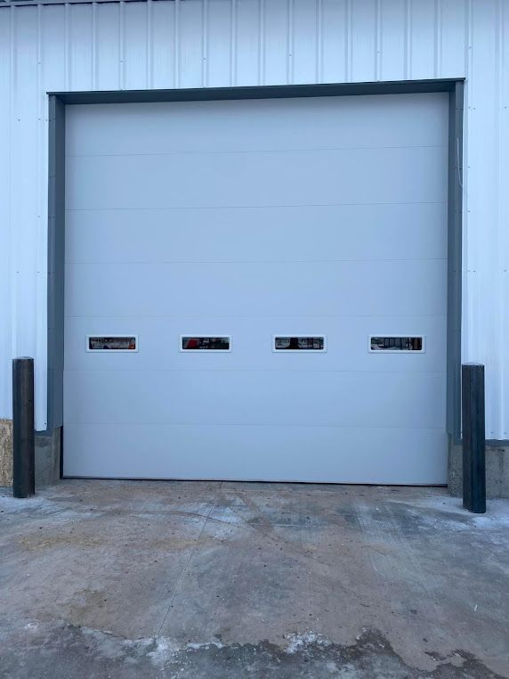Gray industrial garage door with four horizontal windows, framed in gray, between two black posts.