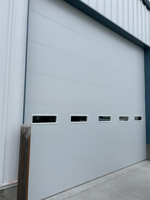 Large, gray commercial overhead door with five rectangular windows, on a light blue building.