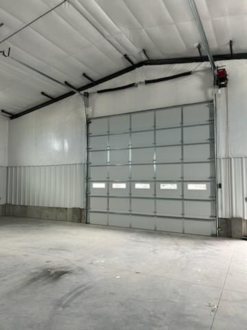 Warehouse interior with a closed, paneled overhead door. Concrete floor, metal walls, and a high ceiling.