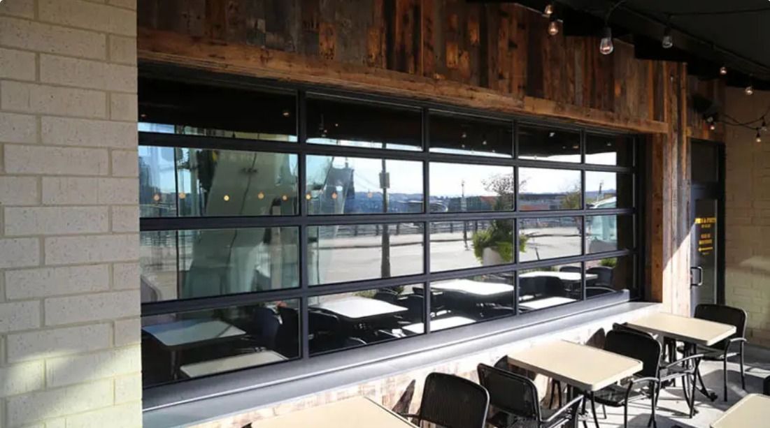 Restaurant interior with a large window overlooking an outdoor area with tables, chairs, and a cityscape.