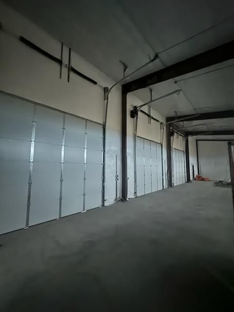 Interior of a warehouse with several closed white garage doors, a concrete floor, and metal beams.
