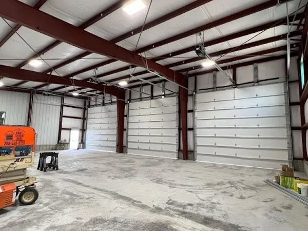 Interior of a large, empty warehouse with three closed garage doors, red steel beams, and a concrete floor.
