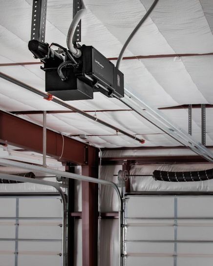 Garage door opener attached to ceiling beams above a closed garage door.