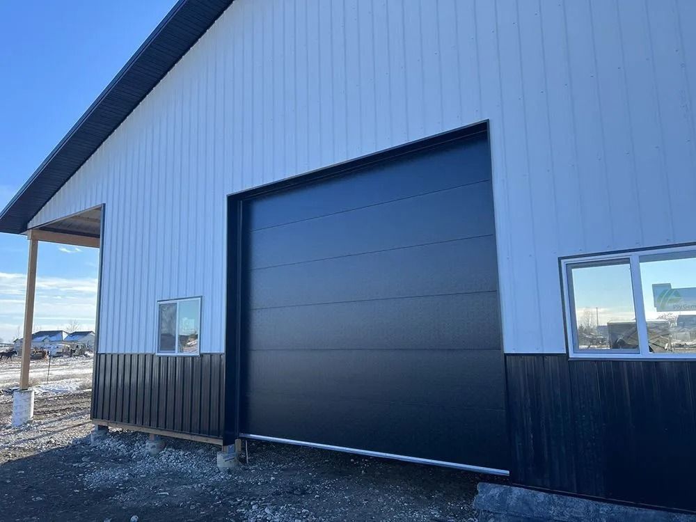 Black and white building with a large black garage door, two small windows, and blue sky.