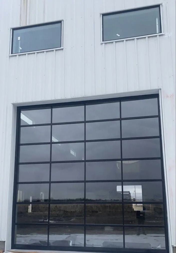 White building with large glass garage door and two rectangular windows.