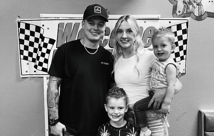 Family of four smiling in front of racing-themed decorations. Black and white photo.