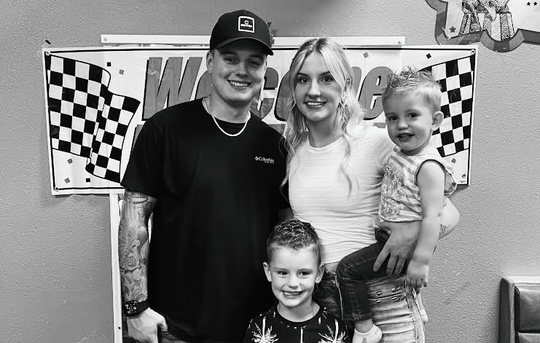 Family of four smiling in front of racing-themed decorations. Black and white photo.
