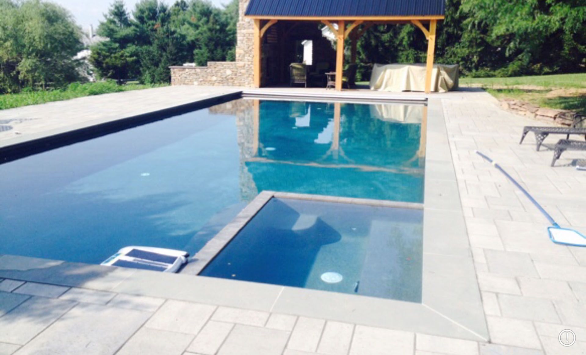 An elegant pool with a paved patio, and wooden pavilion