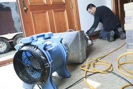 A man is kneeling down next to a fan in a room