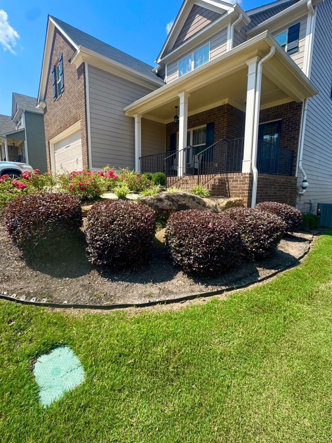 Residential building with burgundy bushes in the foreground, flower bed in the middle, and green lawn on a sunny day.