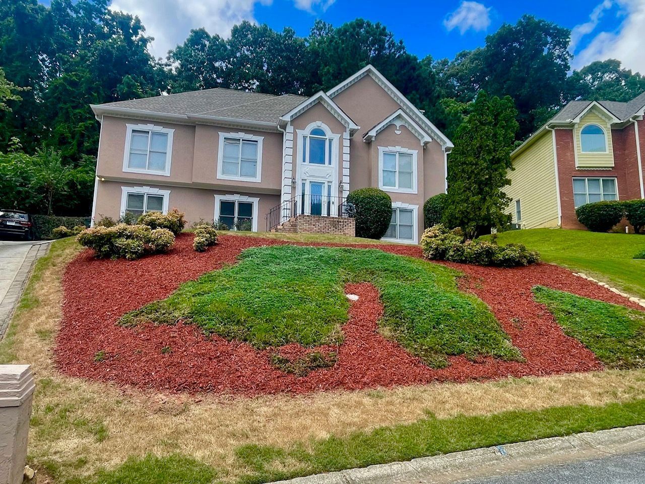 Beige house with red mulch and green grass landscaping. Cloudy sky.