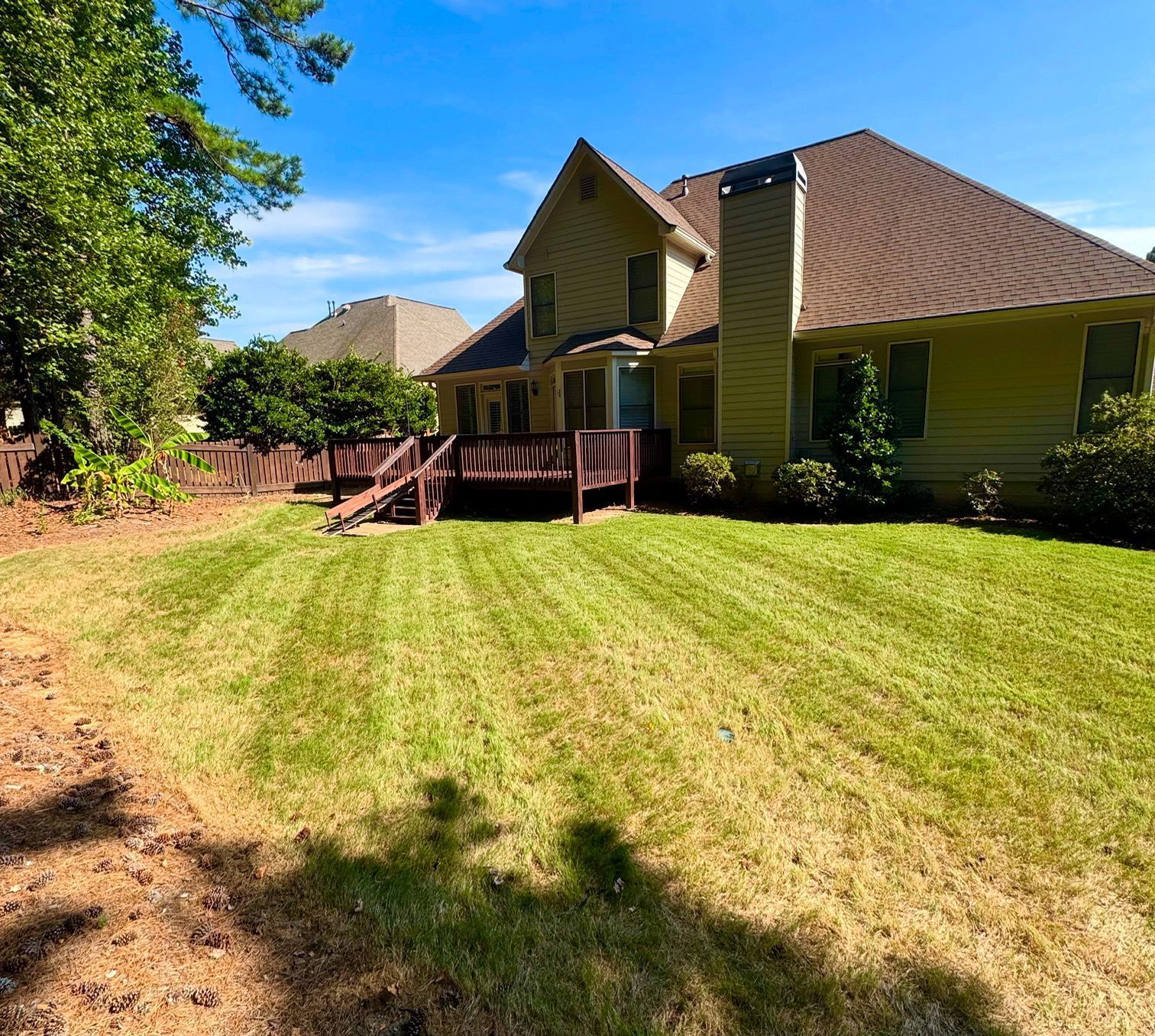 Yellow house with a brown roof and a green lawn under a blue sky.