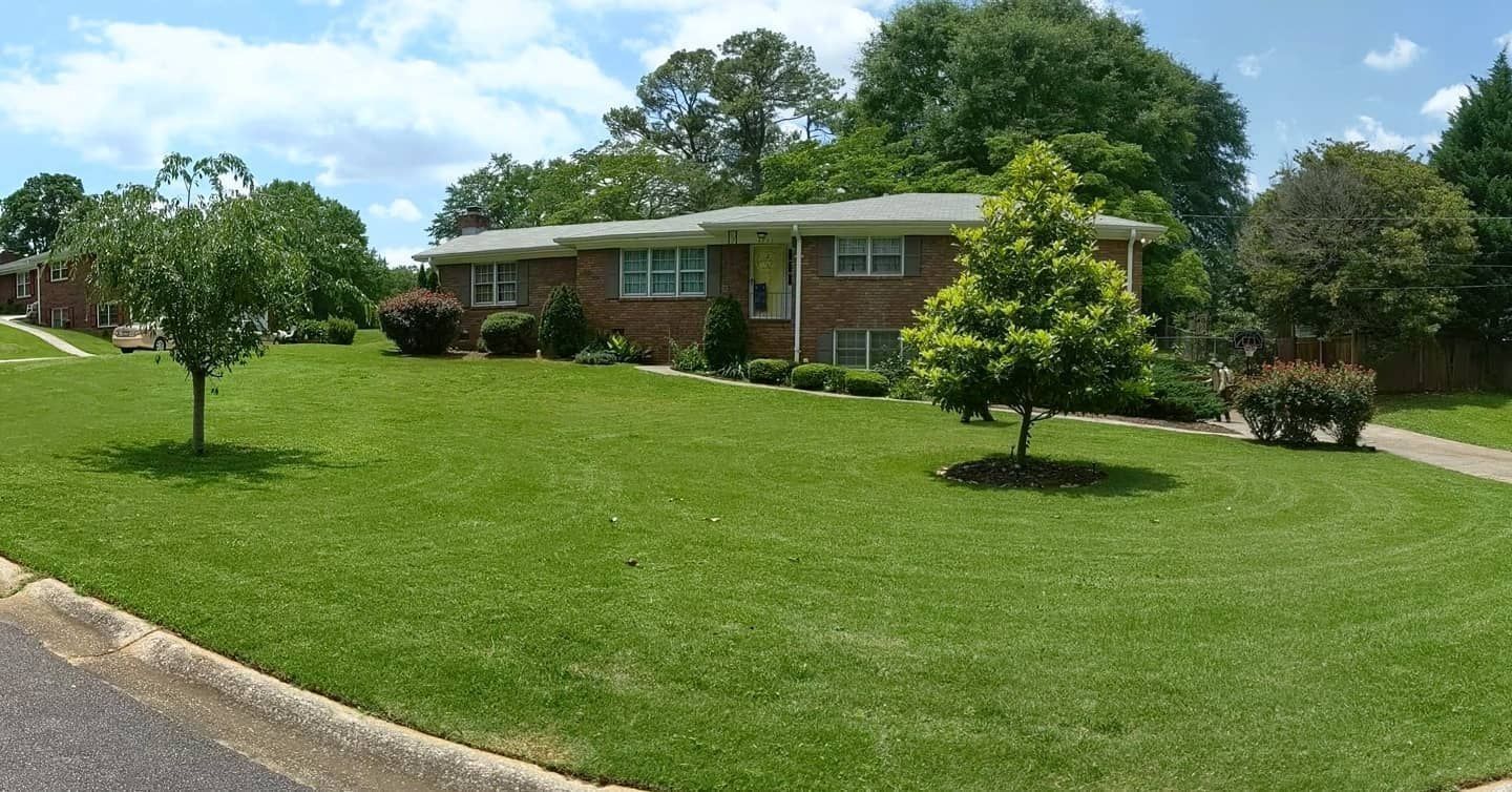Low-rise brick apartments with green lawn and trees on a sunny day.