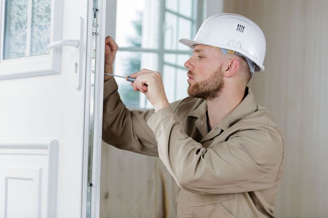 Worker inspecting a white door frame with a tool during home renovation